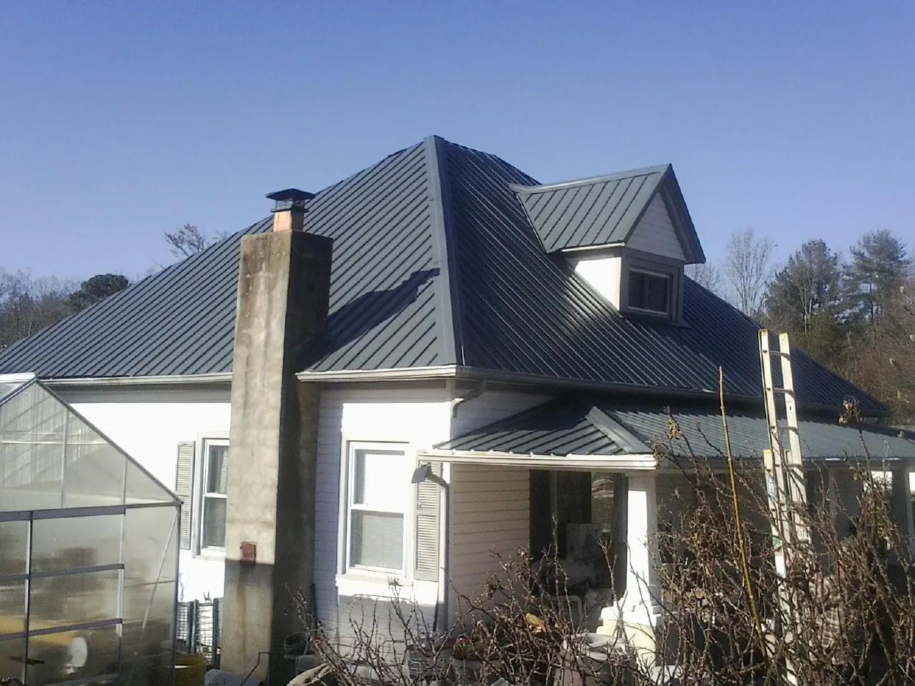 Dark blue standing seam metal roof on a white farmhouse with dormer — Slate & Tile Roof Repair by Roofing Brothers in Woolwine