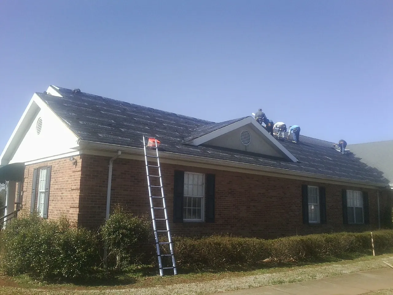 Crew tearing shingles off a brick ranch roof with a ladder set — Metal Roof Repair work by our crew in Woolwine
