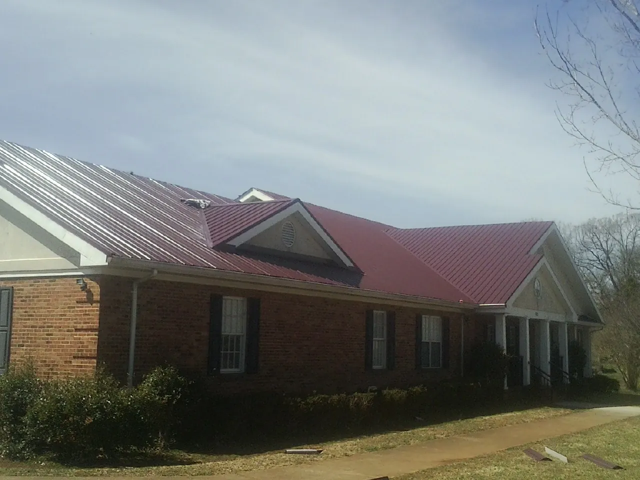 Red metal roof with gabled entries on a long brick building, from a Hail Damage Roof Repair job in Woolwine