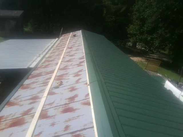Old rusted panels beside newly installed green metal roofing — Wind Damage Roof Repair by Roofing Brothers in Woolwine