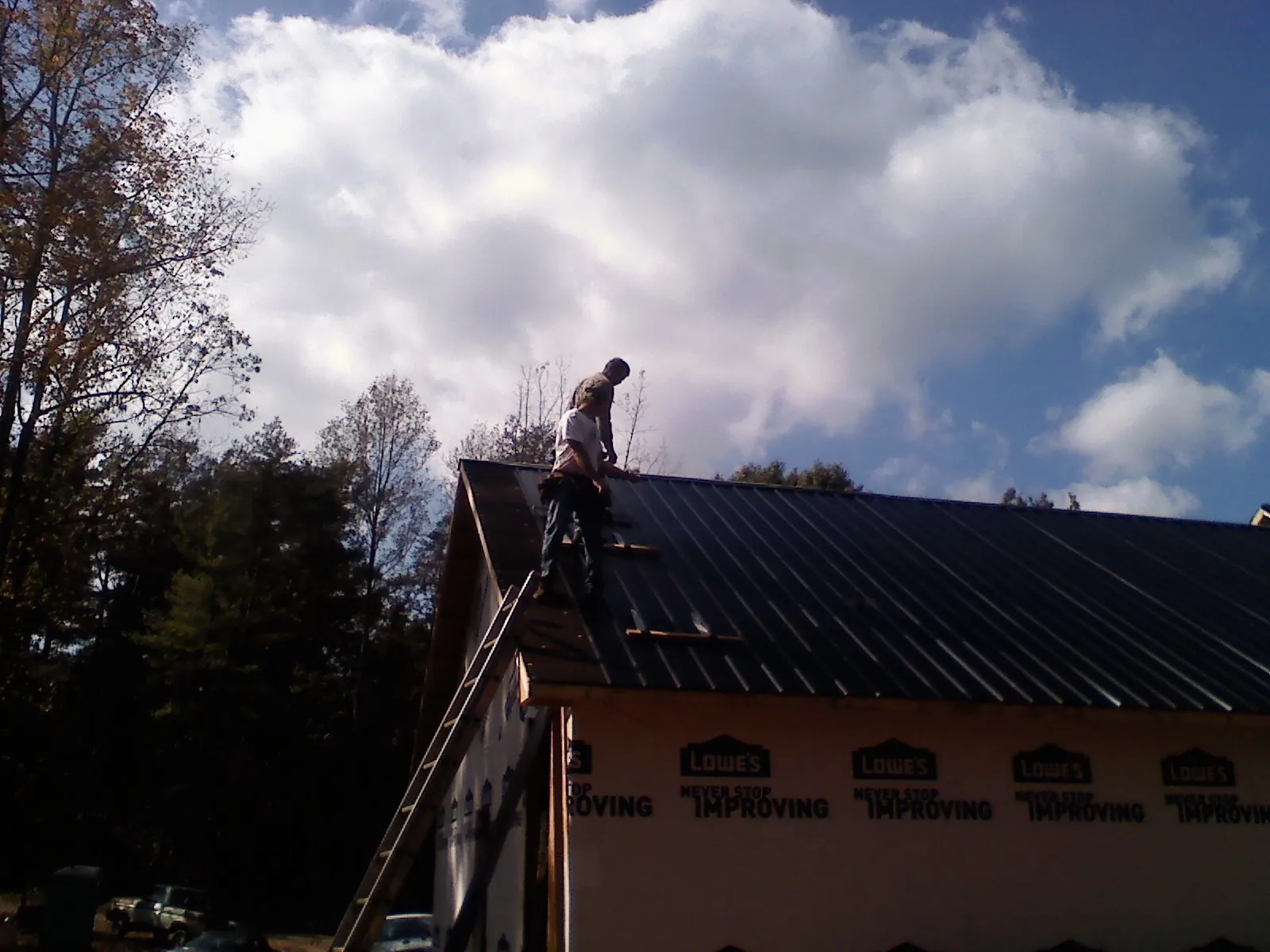 Roofer fastening dark metal panels high against a cloudy sky, from a Roof Inspection job in Woolwine