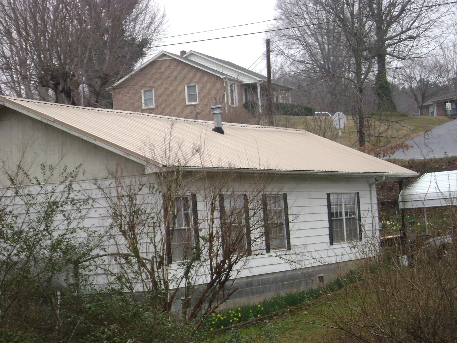 Tan metal roof on a white sided house set into a hillside — Commercial Roofing by Roofing Brothers in Woolwine