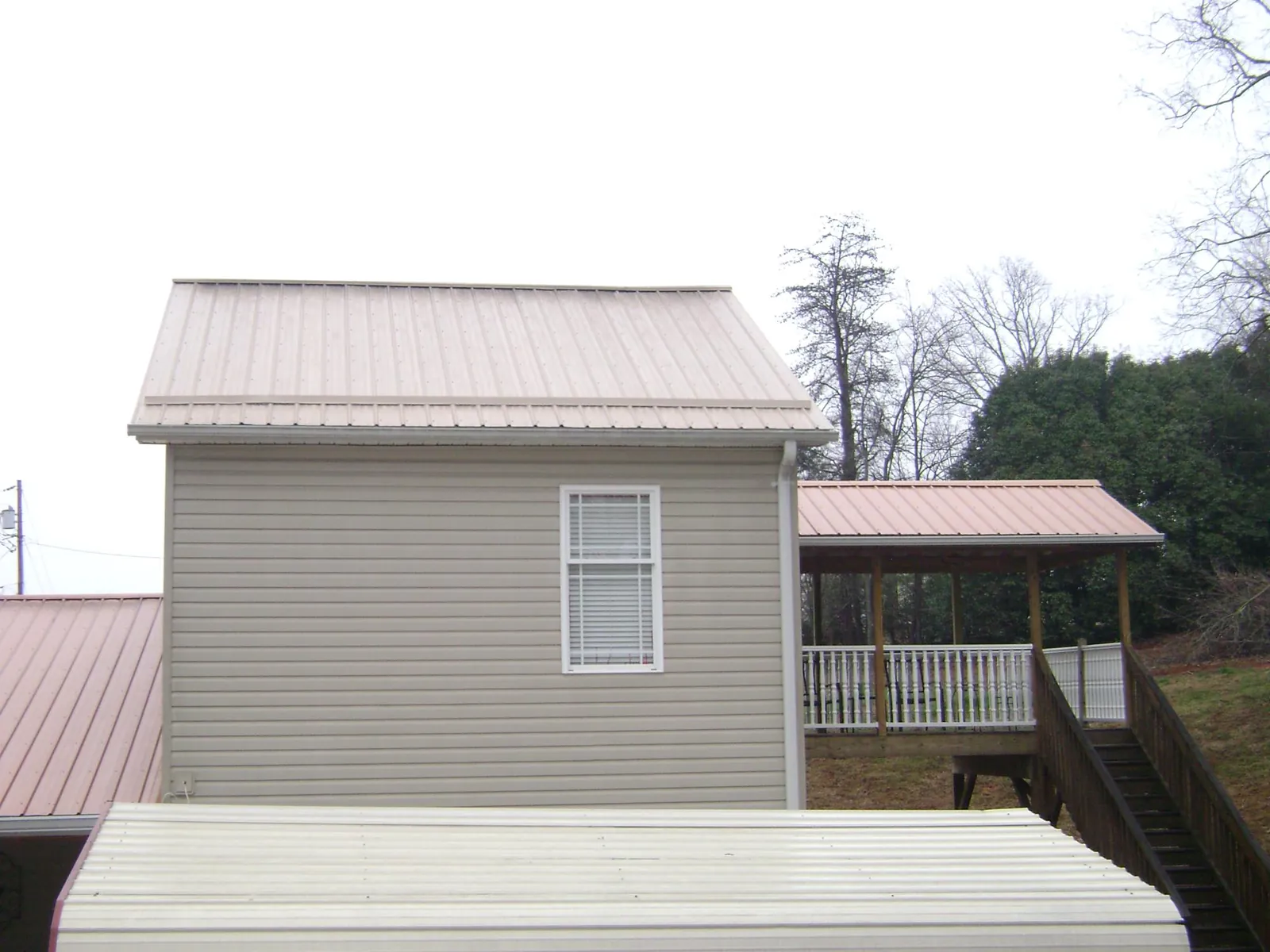 Tan metal roofs on a two story addition and attached porch, from a Roof Replacement job in Woolwine